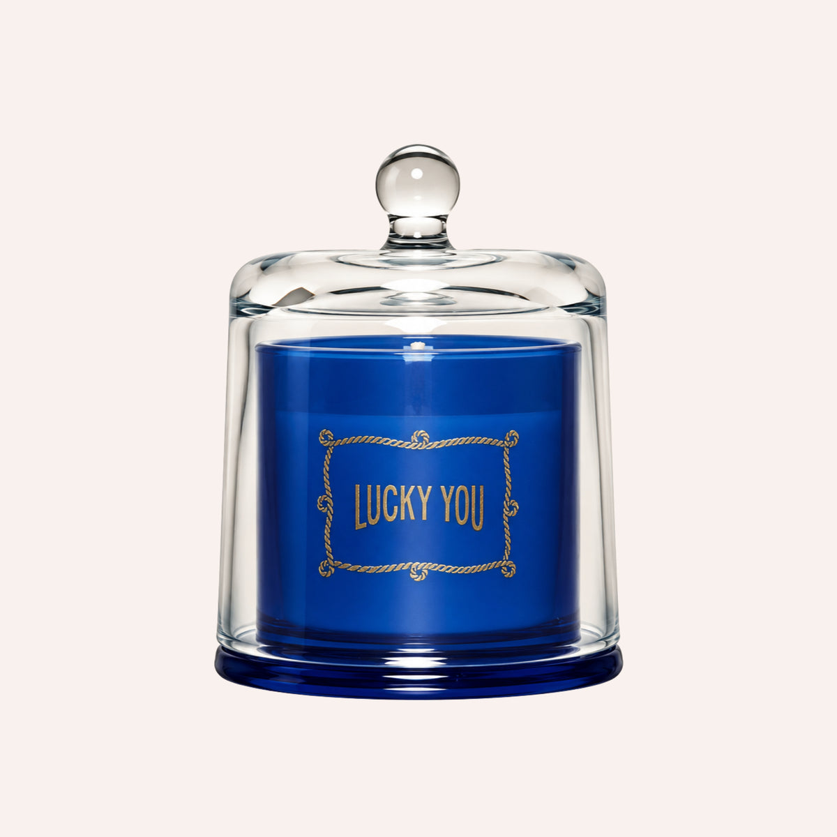 A blue candle under a clear glass cloche with a round knob lid, featuring gold foil text that reads 'LUCKY YOU' on the front.