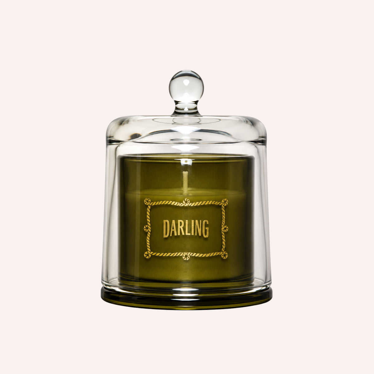 A green candle in a clear glass jar with a matching glass dome lid and a gold 'DARLING' label on the front, set against a solid off-white background.