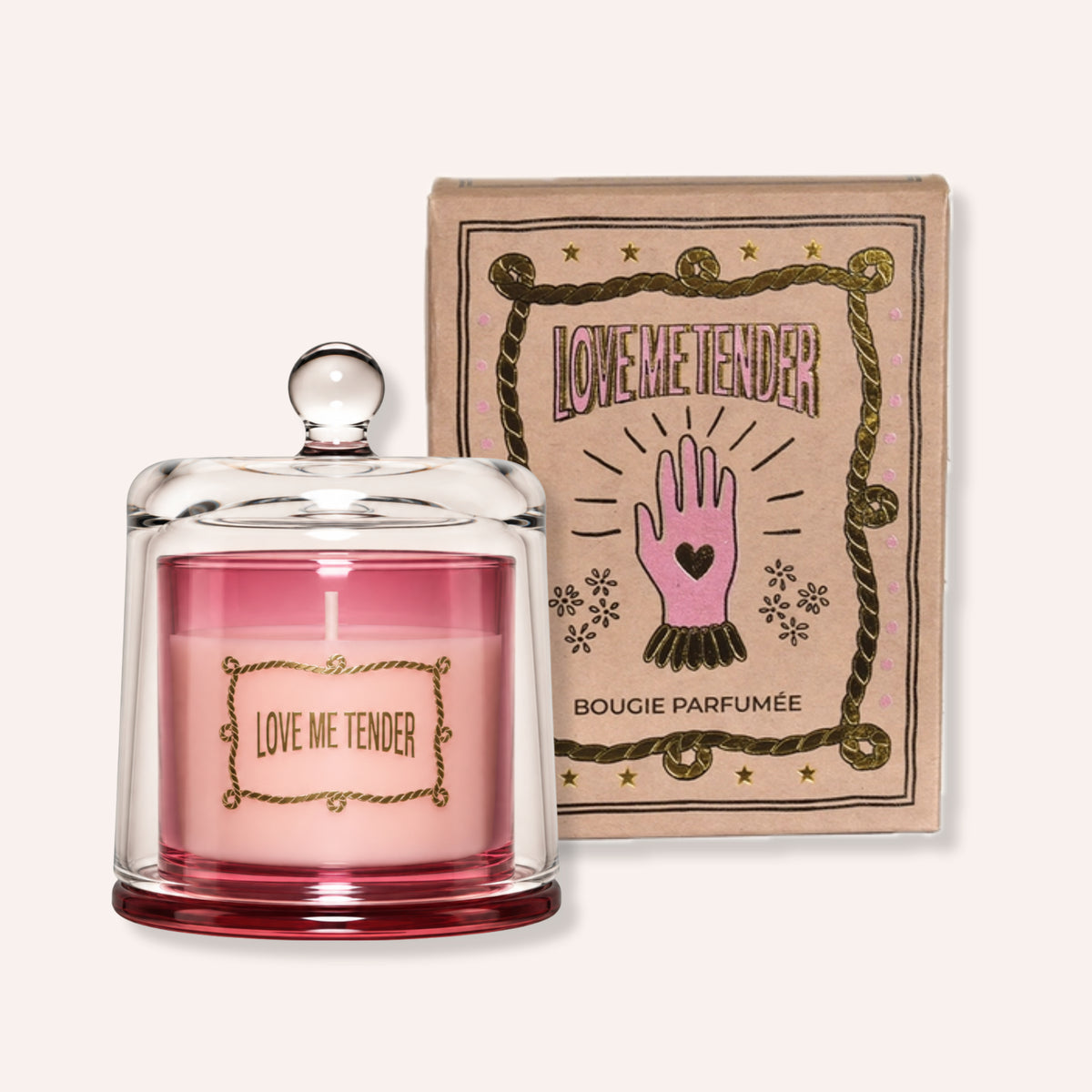 A pink scented candle in a clear glass jar with a glass lid sits in front of its kraft paper packaging box. The box features a pink hand graphic and the text 'LOVEME TENDER' and 'BOUGIE PARFUMÉE'.