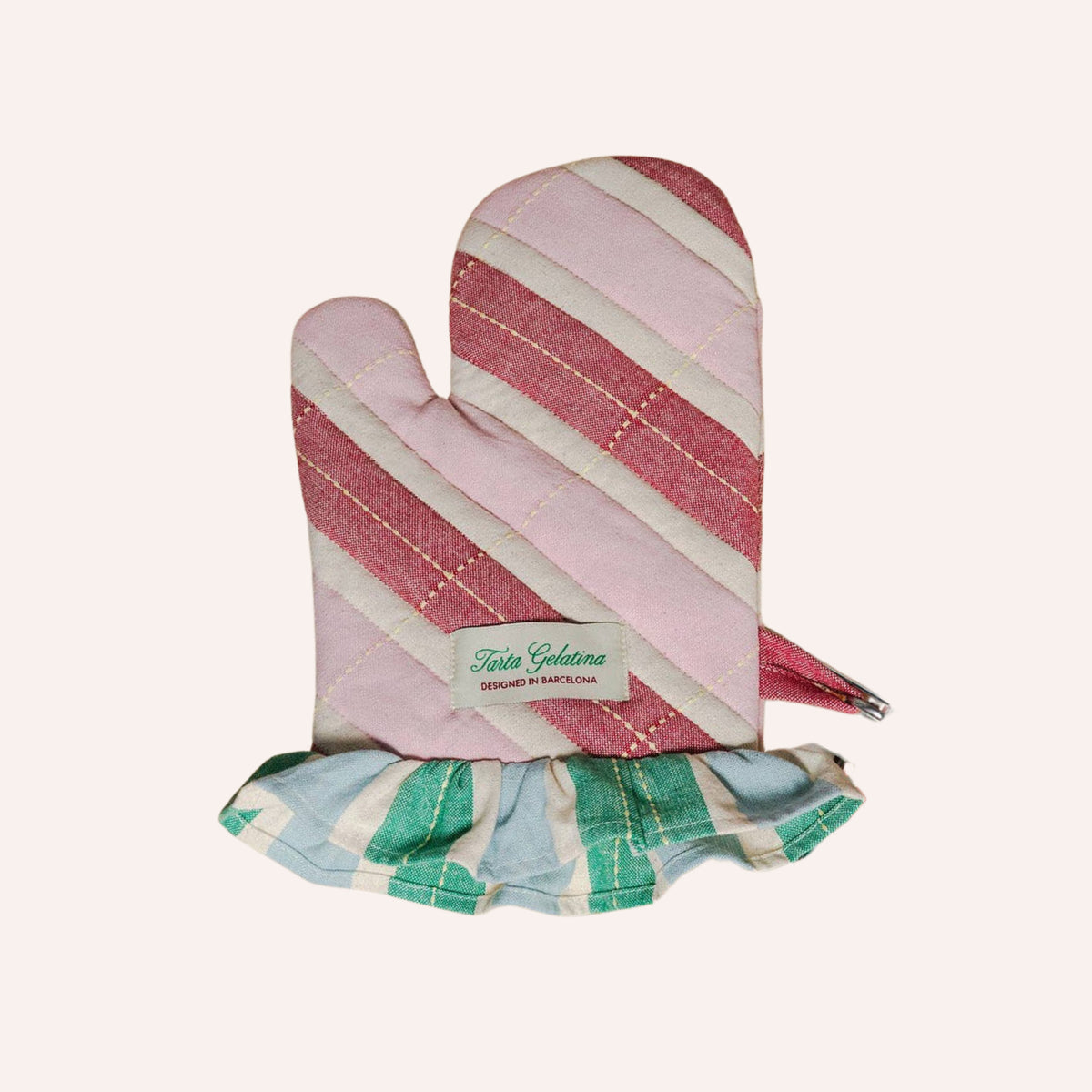 A quilted oven mitt with diagonal pink and cream stripes, featuring a ruffled trim at the bottom in green, blue, and cream stripes, with a visible 'tarta gelatina' brand label.